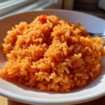 A close-up of fluffy, orange-colored Spanish Rice served in a white bowl, ready to eat.