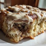 A close-up of a single, gooey Biscoff Cookie Butter Cinnamon Rolls slice topped with thick, light brown icing and nuts.