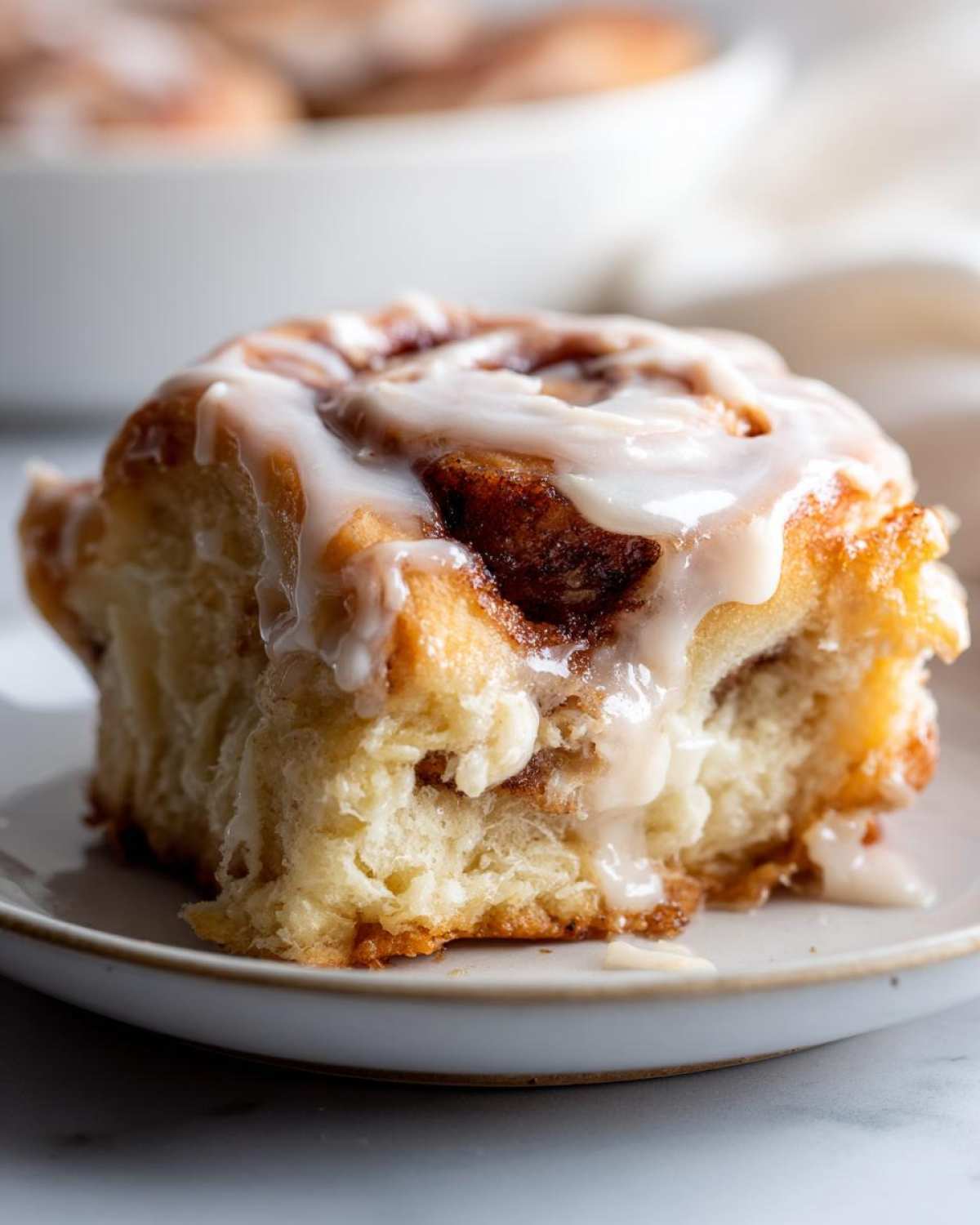 A close-up of a fluffy, iced Biscoff Cookie Butter Cinnamon Rolls slice on a small plate.