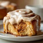A close-up of a single, fluffy Biscoff Cookie Butter Cinnamon Roll topped with a thick, dripping Biscoff glaze.