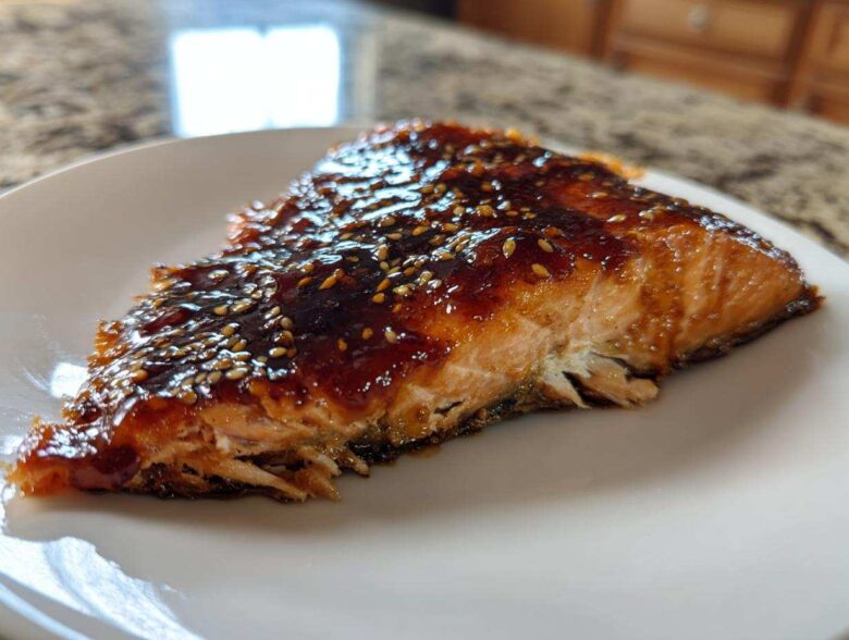 A close-up of a perfectly cooked salmon fillet topped with shiny Brown Sugar Teriyaki Salmon Glaze and sesame seeds.