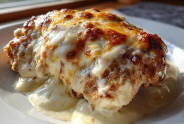 A close-up of a piece of Cheesy Baked Chicken with Cream Sauce, topped with melted, browned cheese.