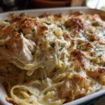 A spoonful of Cheesy Chicken Alfredo Bake with Creamy Sauce being lifted from a white baking dish, showing melted cheese pull.
