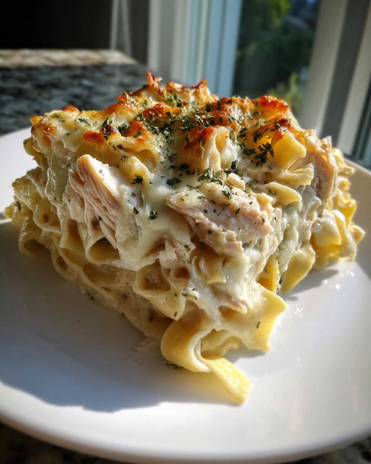 A generous serving of Cheesy Chicken Alfredo Bake with Mozzarella featuring baked, browned cheese and parsley.