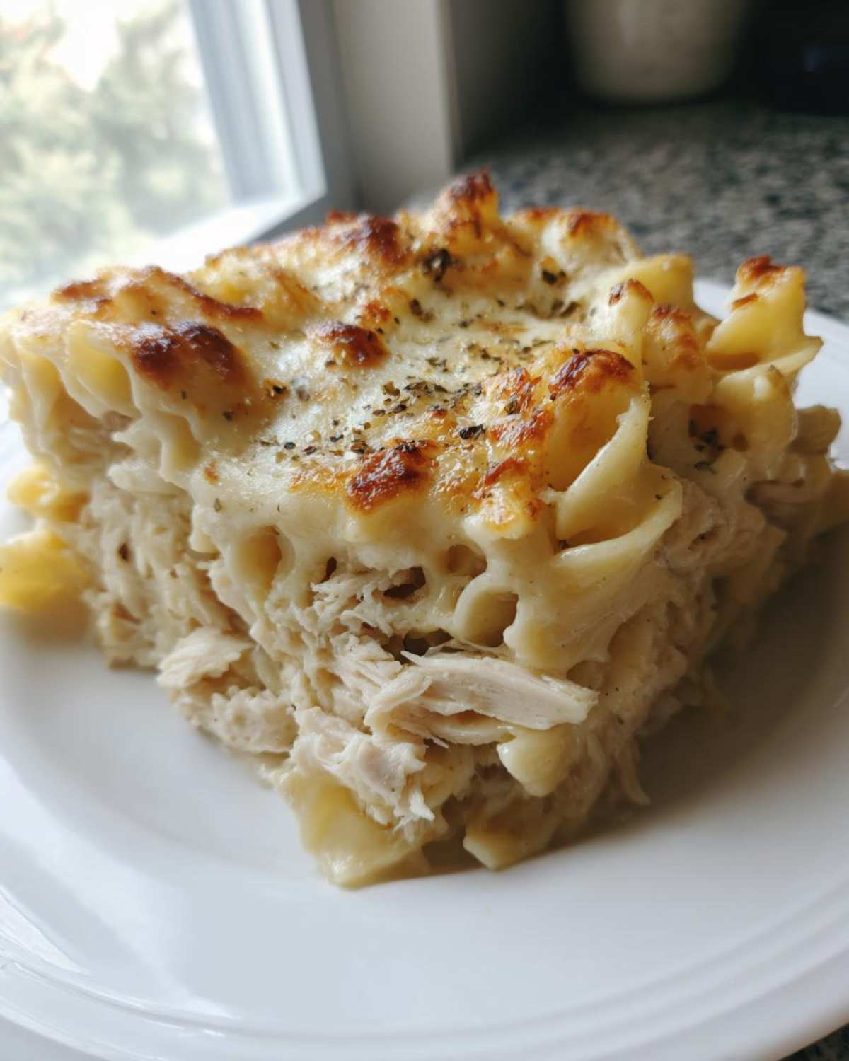 A close-up slice of Cheesy Chicken Alfredo Bake with Mozzarella showing shredded chicken and pasta under a bubbly, browned cheese topping.
