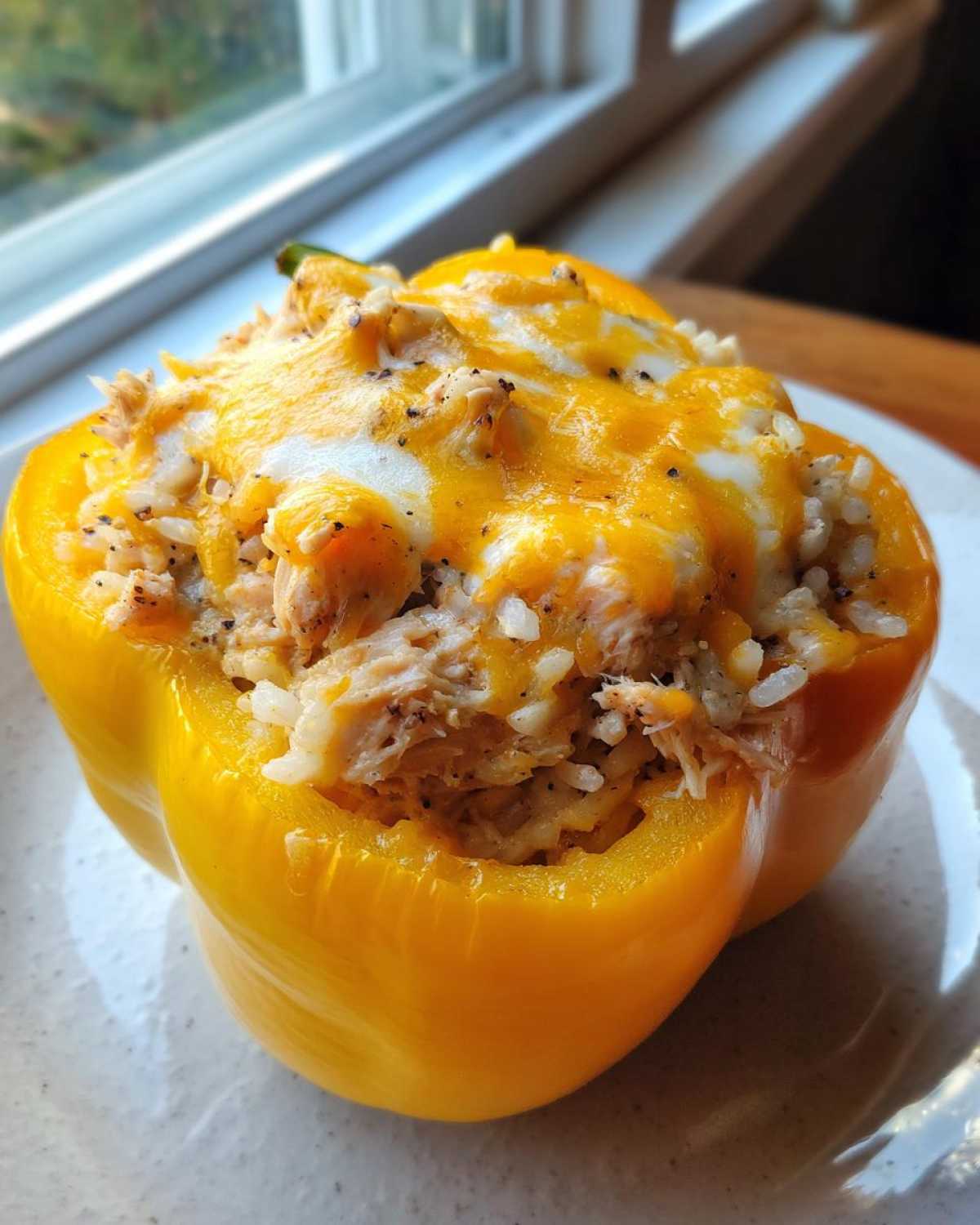 A bright yellow bell pepper stuffed with chicken, rice, and melted cheddar cheese, ready to eat.