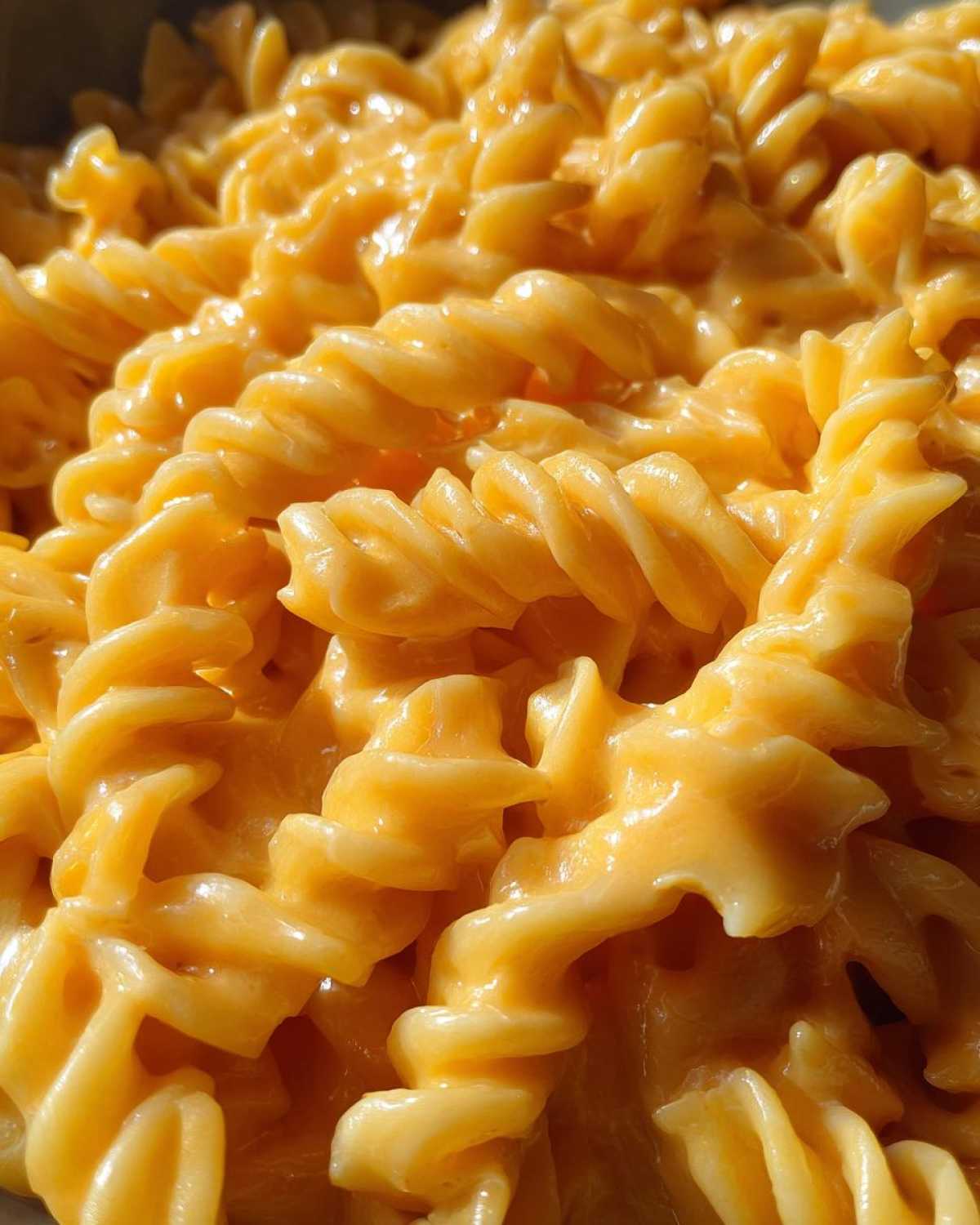 Extreme close-up of rotini pasta coated in a rich, orange, creamy sauce, representing Cheesy Chicken Pasta with Creamy Sauce.