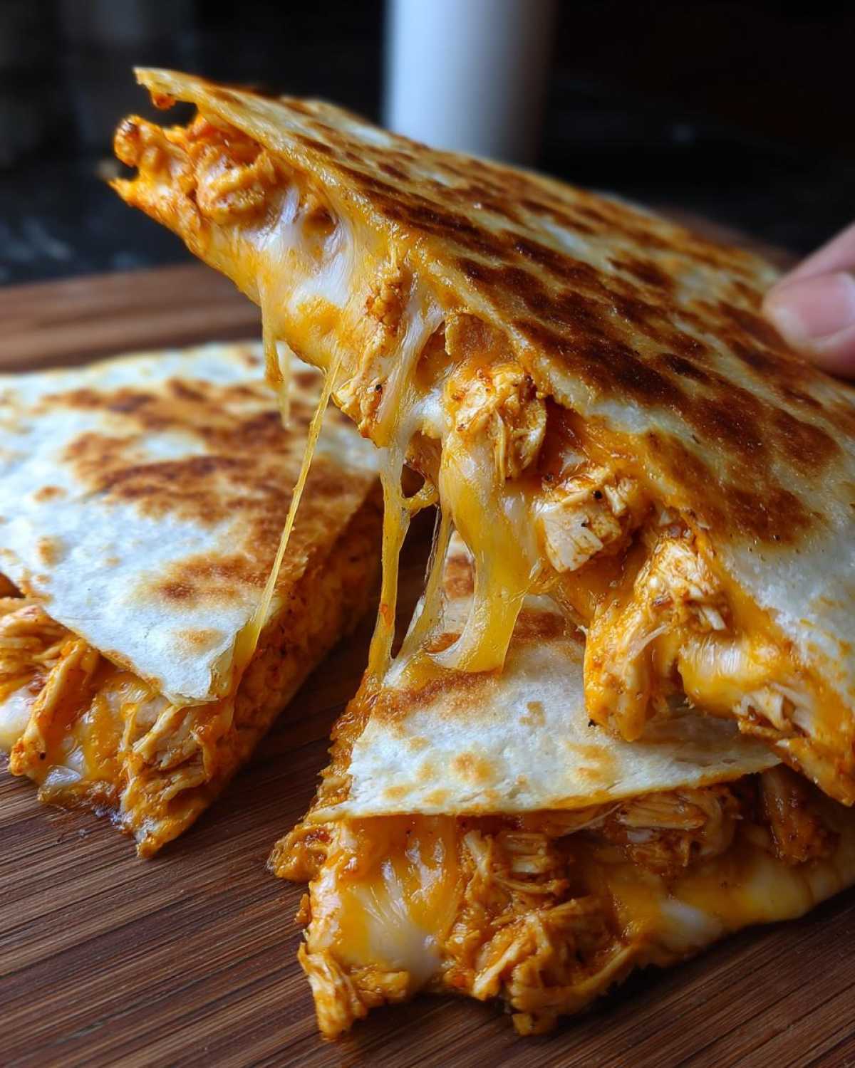 Close-up of a Cheesy Chicken Quesadilla with Crispy Tortilla being pulled apart, showing long strings of melted orange cheese and shredded chicken.