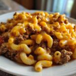 A close-up of Cheesy Ground Beef Pasta Skillet Comfort Food served on a white plate, featuring elbow macaroni and melted cheddar cheese.