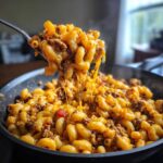 A spoonful of Cheesy Ground Beef Pasta Skillet Comfort Food showing a dramatic cheese pull over the skillet.