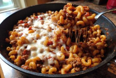 A spoonful of Cheesy Ground Beef Pasta Skillet showing a dramatic mozzarella cheese pull from the skillet.