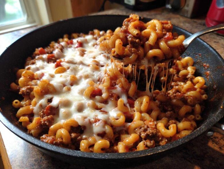 A spoonful of Cheesy Ground Beef Pasta Skillet showing a dramatic mozzarella cheese pull from the skillet.