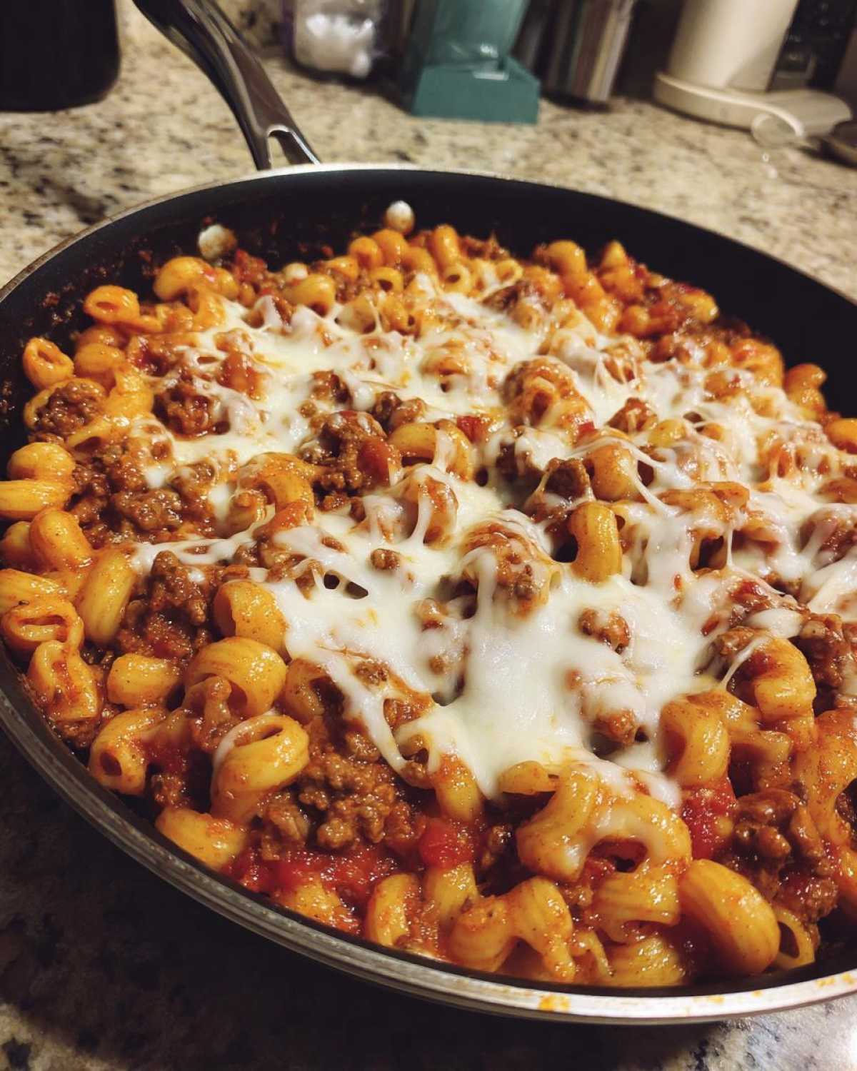 Close-up of Cheesy Ground Beef Pasta Skillet in a black pan, topped with melted mozzarella cheese.