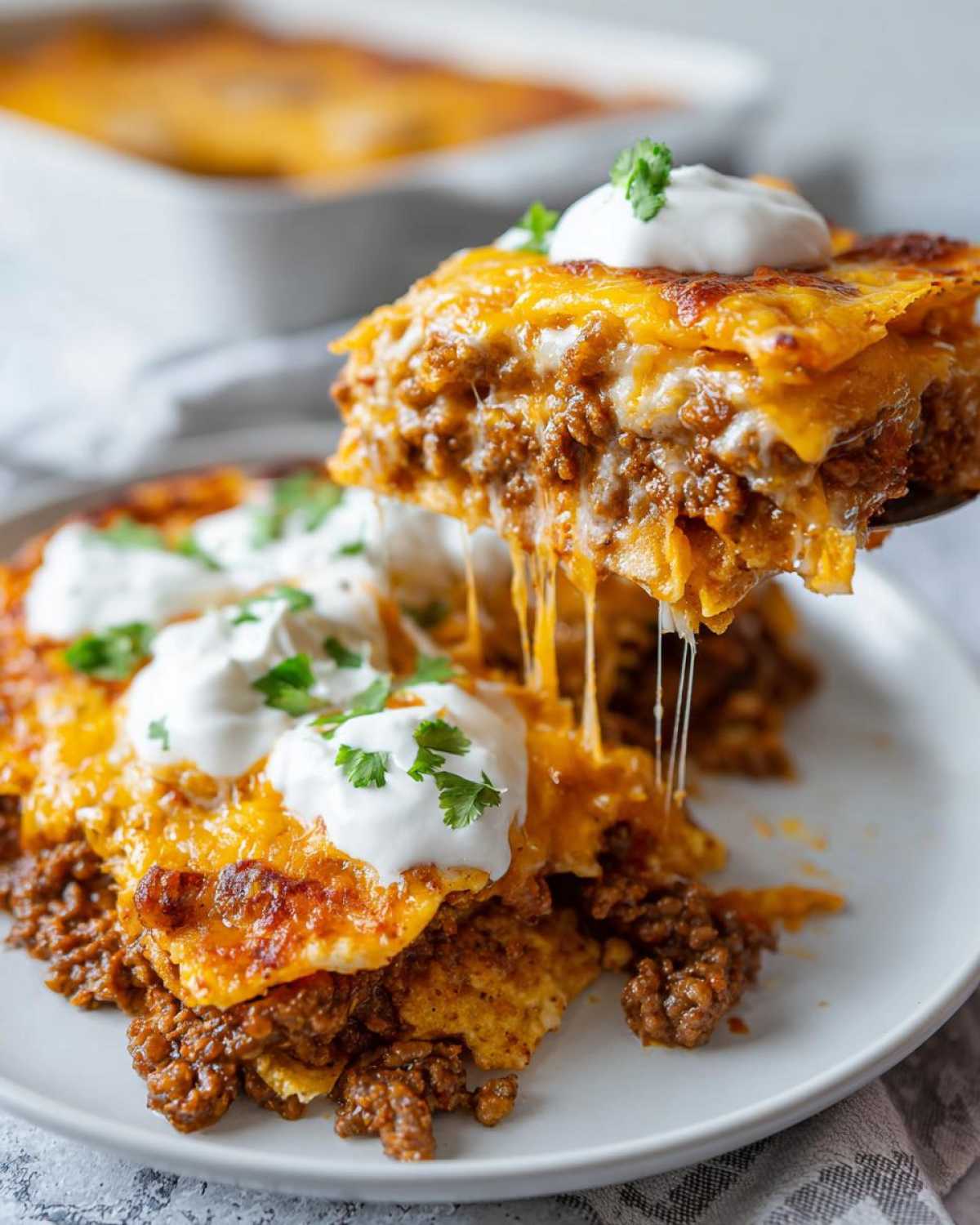 A spoonful of Cheesy Ground Beef Queso Bake showing melted cheese strings, topped with sour cream and cilantro.