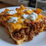 A generous slice of Cheesy Ground Beef Queso Bake Comfort Dish topped with melted cheese, sour cream dollops, and tortilla chips.