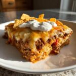 A hearty slice of Cheesy Ground Beef Queso Bake Comfort Dish topped with melted cheese, sour cream, and tortilla chips.