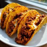 Four crispy tacos filled with seasoned ground beef, melted cheese, and a creamy white sauce, ready to eat.
