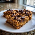 Three chewy Banana Oats Bars topped with melted chocolate chips served on a white plate.