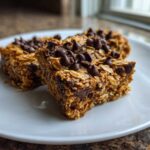 Three chewy Banana Oats Bars, rich with oats and topped generously with chocolate chips, served on a white plate.