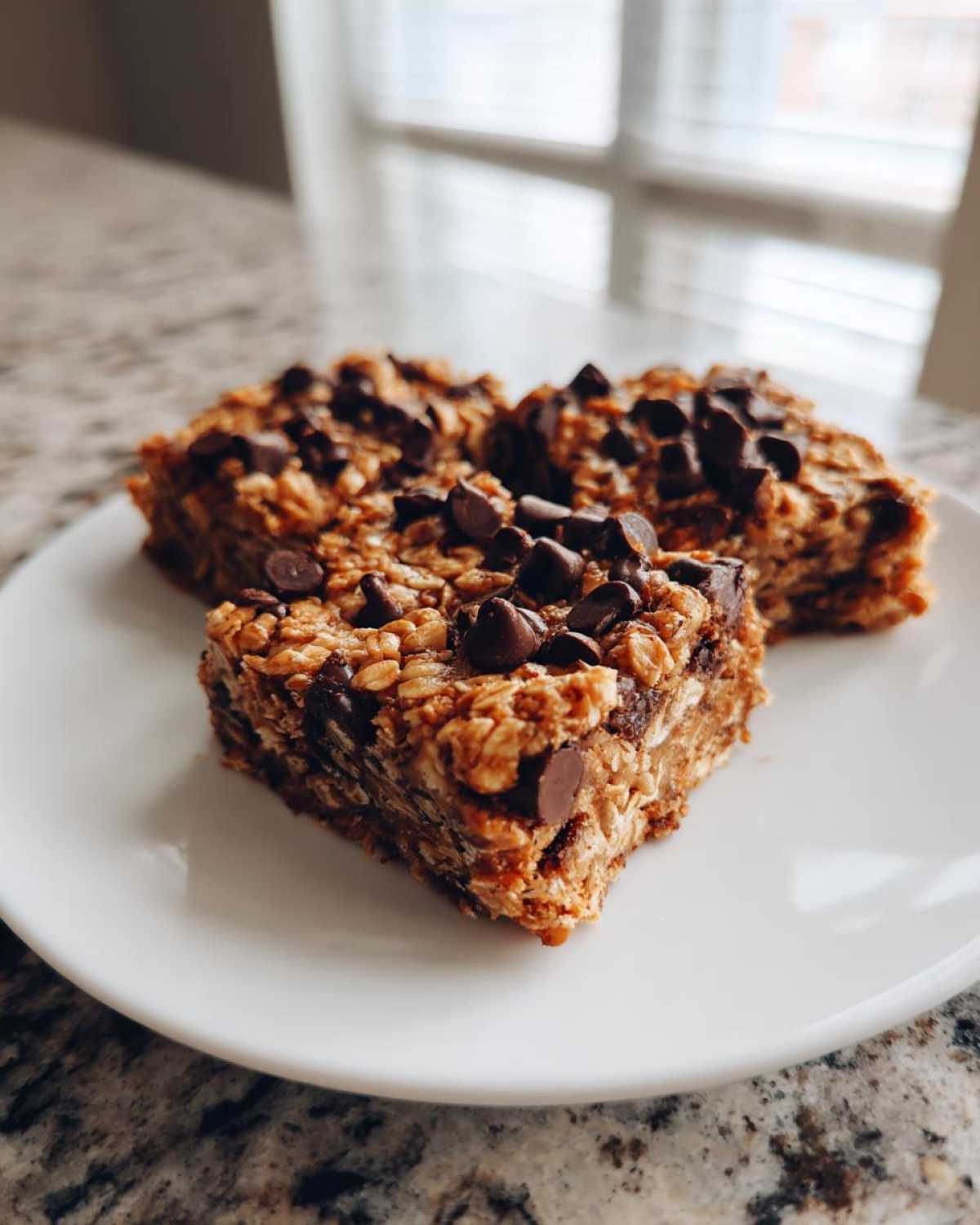 Three chewy Banana Oats Bars topped with chocolate chips resting on a white plate.