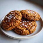 Close-up of three golden brown Chewy Salted Honey Cookies topped with flaky sea salt.