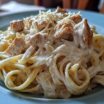 A close-up shot of rich, creamy Alfredo chicken pasta topped with shredded Parmesan cheese.
