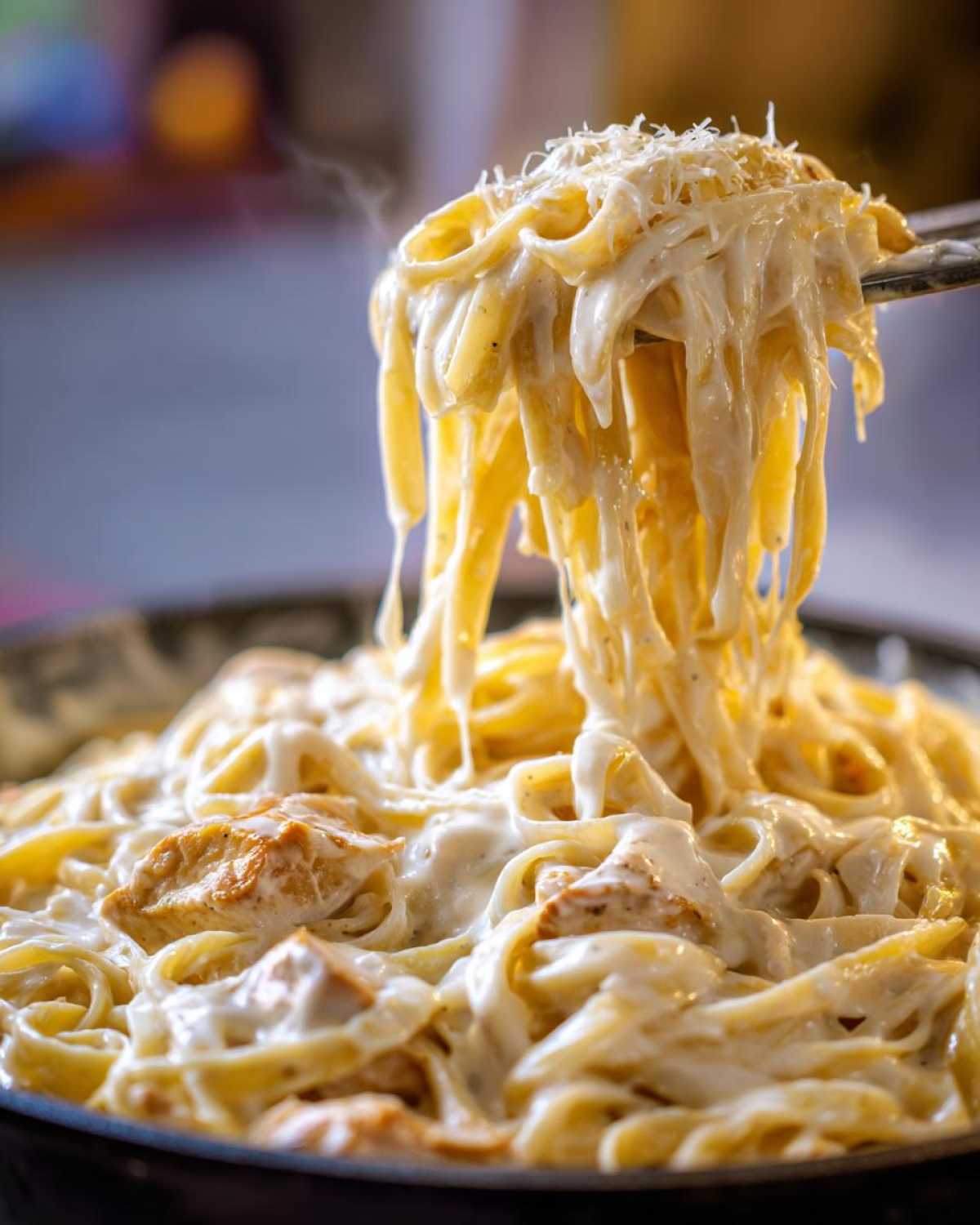 Close-up of steaming fettuccine noodles coated in rich sauce being lifted from a pan of Creamy Alfredo Chicken Pasta.