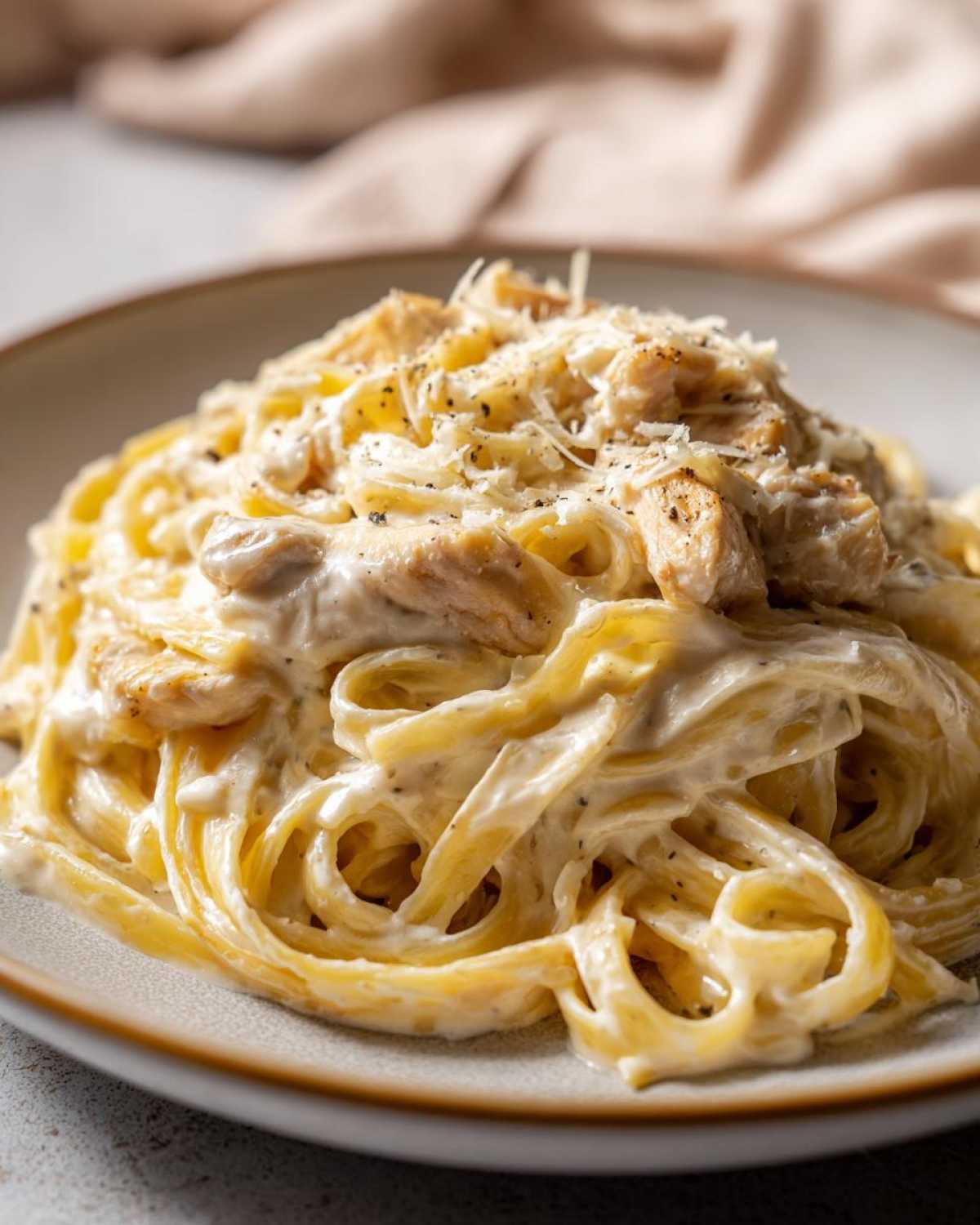 A close-up shot of Creamy Alfredo Chicken Pasta featuring fettuccine noodles coated in rich sauce, topped with chicken pieces and grated Parmesan cheese.