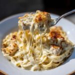 A fork lifts a cheesy bite of Creamy Cajun Chicken Alfredo Bake, showing long, melted cheese strings.