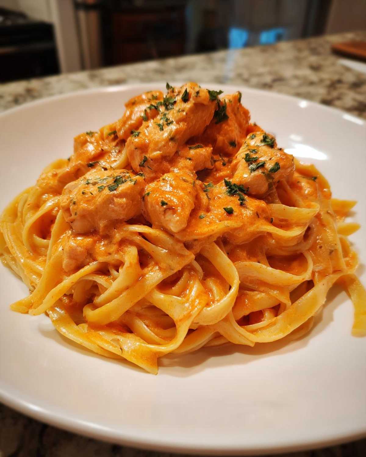 A close-up of a white bowl filled with Creamy Cajun Chicken Pasta, featuring fettuccine noodles and chunks of chicken in a rich, orange sauce.