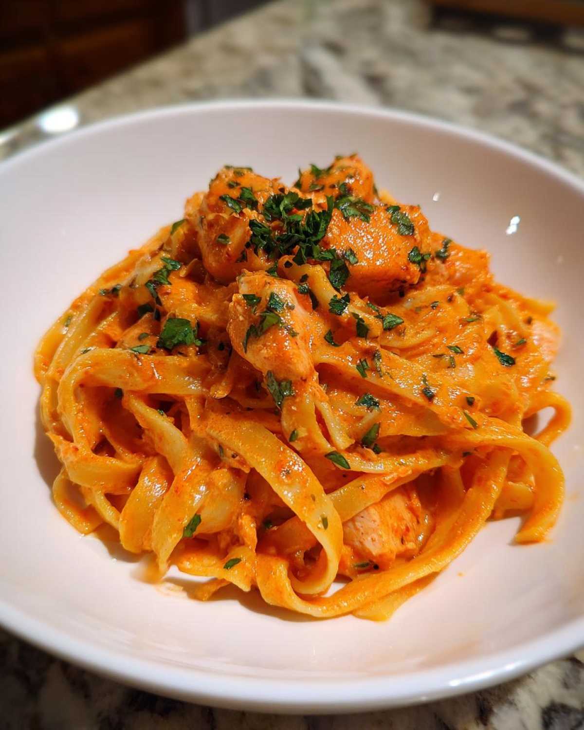 Close-up of Creamy Cajun Chicken Pasta with fettuccine noodles coated in an orange sauce and topped with chicken pieces and fresh parsley.