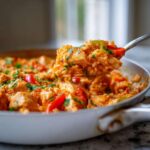 A spoonful of creamy Cajun chicken skillet with rice, red peppers, and parsley being lifted from the pan.