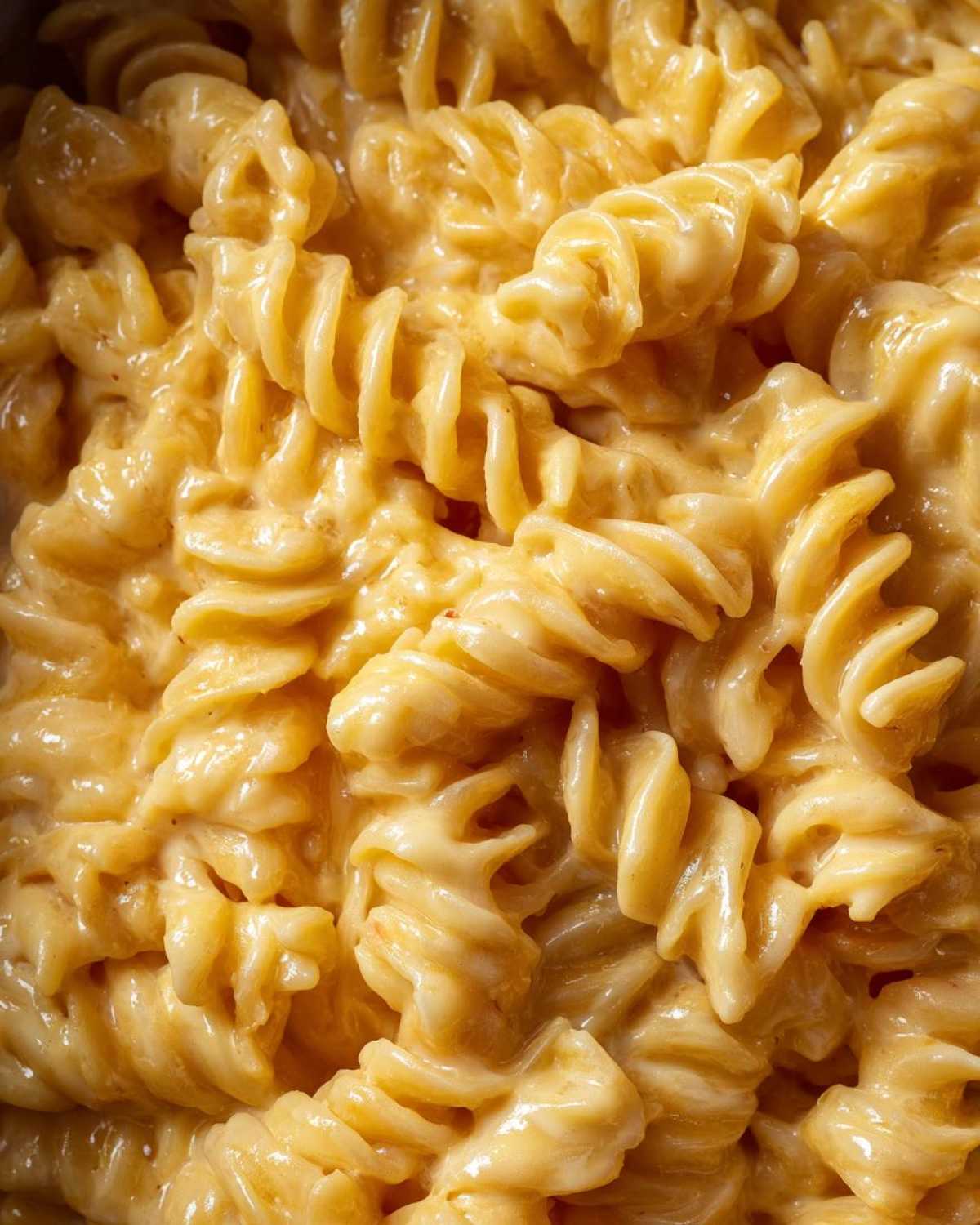 Extreme close-up of fusilli pasta coated in a thick, creamy, cheesy sauce, part of the Cheesy Chicken Pasta with Creamy Sauce recipe.