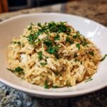 A close-up of Creamy Garlic Parmesan Orzo with Chicken, topped generously with fresh chopped parsley, served in a white bowl.