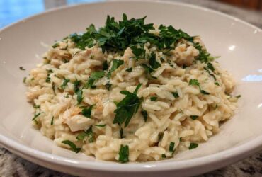 A close-up of creamy Garlic Parmesan Orzo with Chicken, topped generously with fresh chopped parsley in a white bowl.