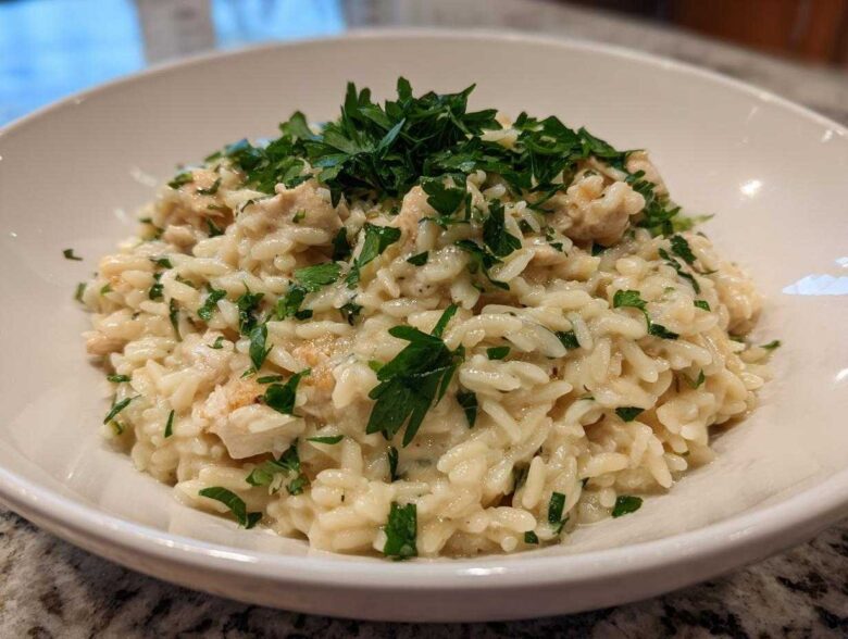 A close-up of creamy Garlic Parmesan Orzo with Chicken, topped generously with fresh chopped parsley in a white bowl.