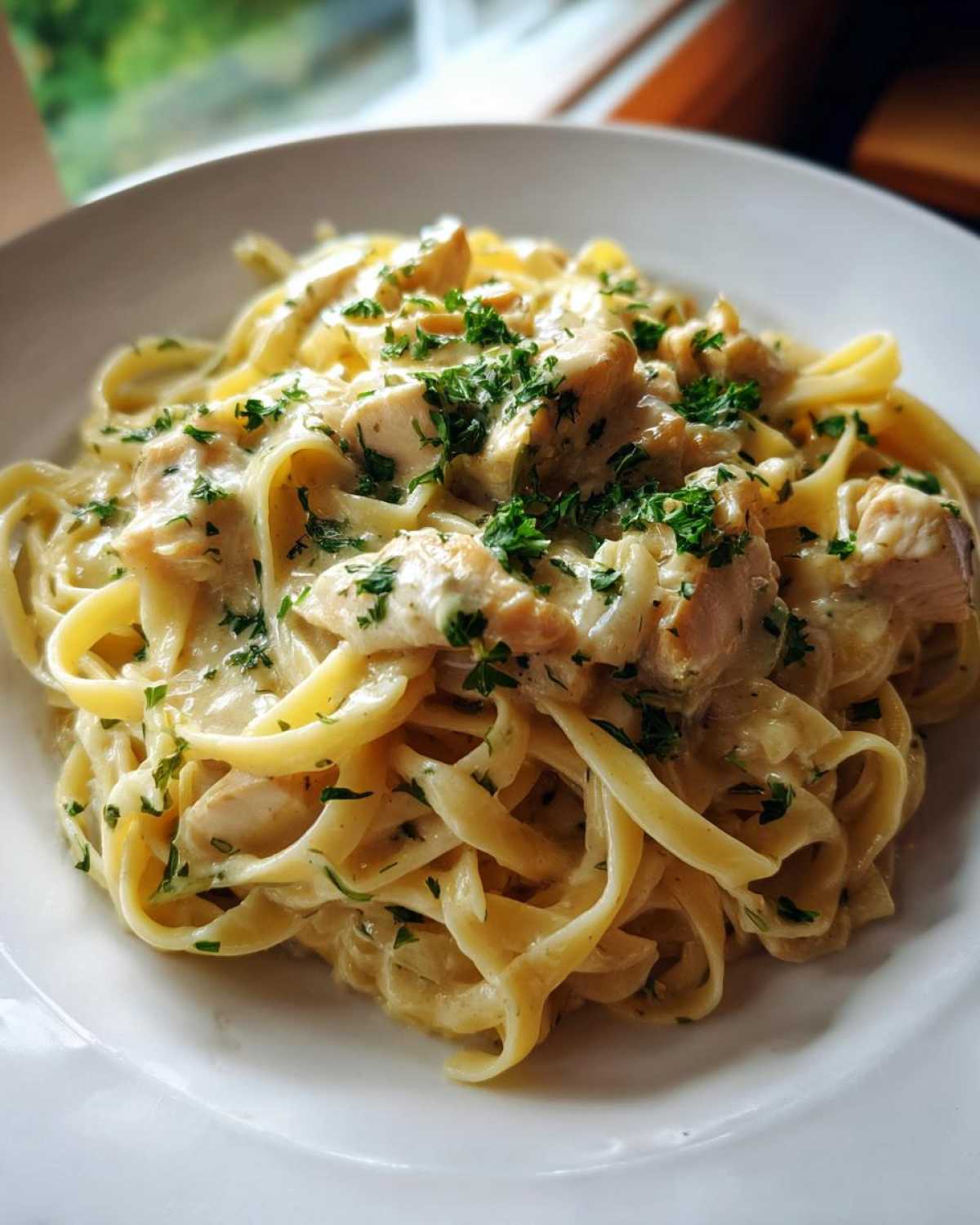 Close-up of fettuccine in a rich sauce with chunks of chicken, garnished with parsley, ready to eat Creamy Lemon Garlic Pasta with Chicken.