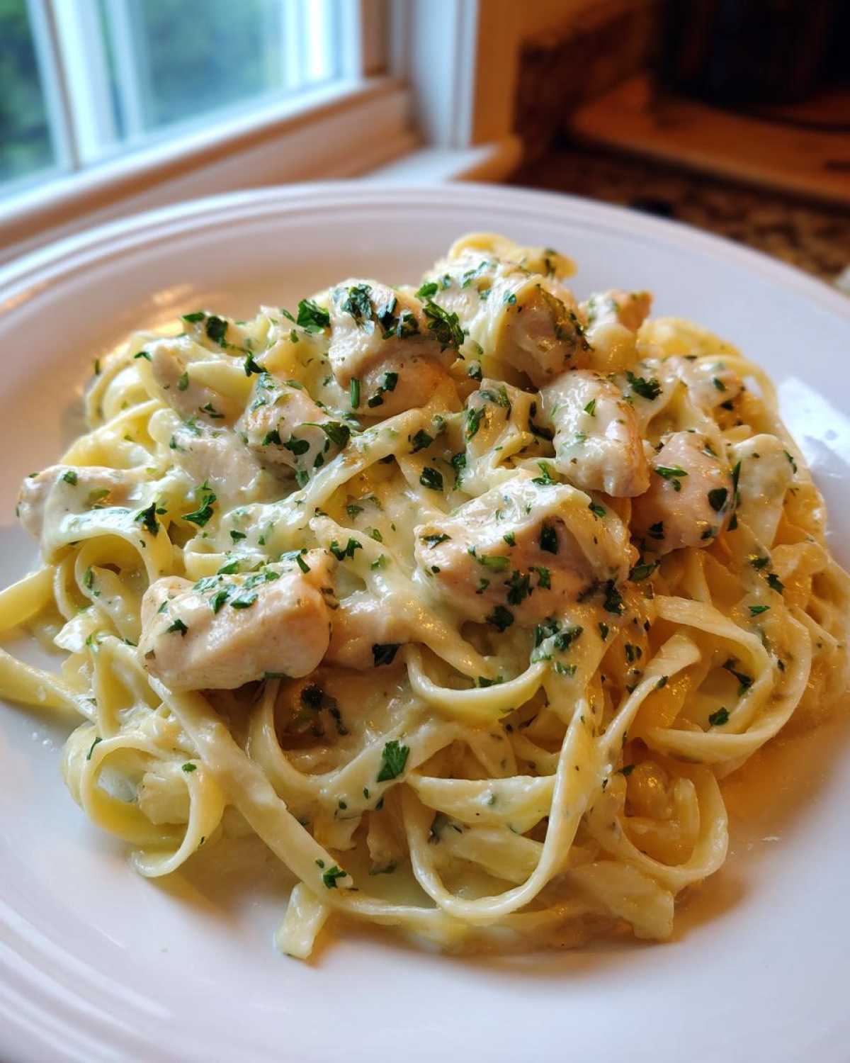 Close-up of fettuccine pasta tossed in a creamy sauce with chunks of chicken and topped with fresh parsley, a serving of Creamy Lemon Garlic Pasta with Chicken.