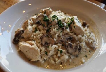 A serving of Creamy Mushroom Chicken and Rice Skillet in a white bowl, topped with parsley.