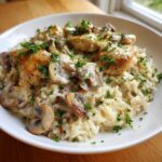 A close-up of a white bowl filled with Creamy Mushroom Chicken and Rice Skillet, topped with fresh parsley.