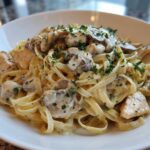 A close-up of a white bowl filled with Creamy Mushroom Chicken Pasta with Garlic Sauce, garnished with fresh parsley.