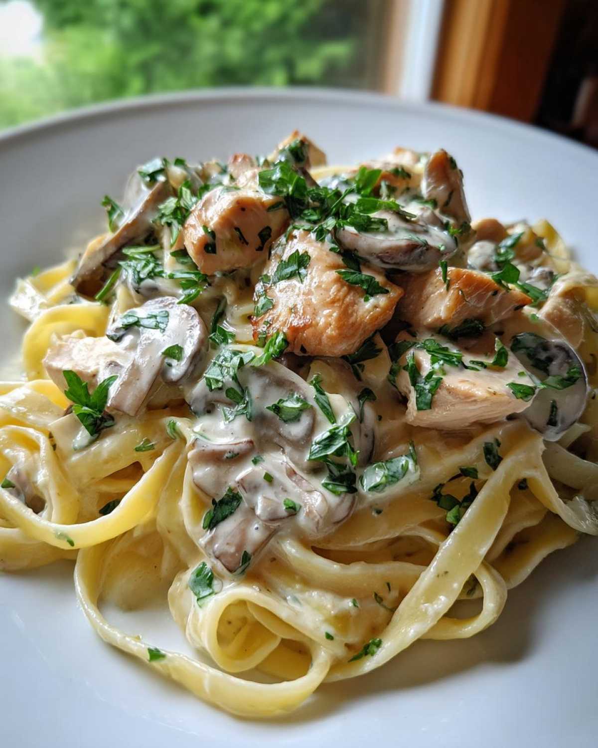 Close-up of creamy mushroom chicken pasta featuring fettuccine noodles coated in garlic sauce, topped with chicken pieces and fresh parsley.