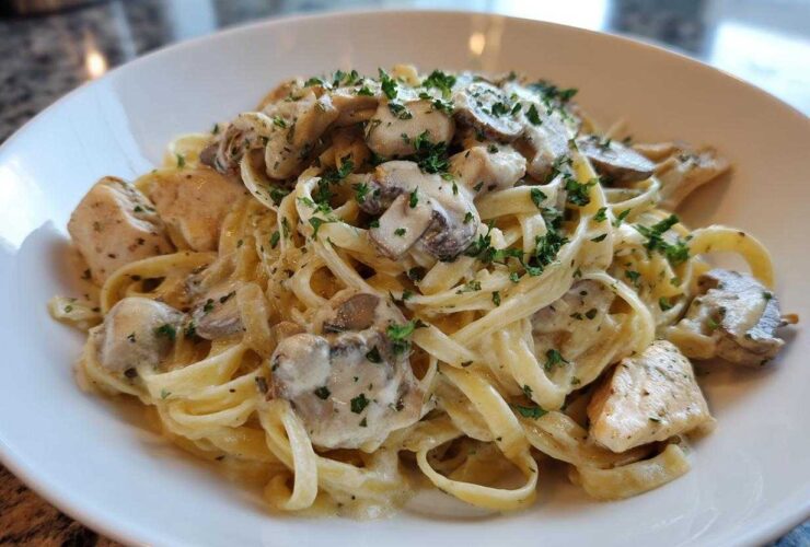 A close-up of a white bowl filled with Creamy Mushroom Chicken Pasta with Garlic Sauce, garnished with fresh parsley.