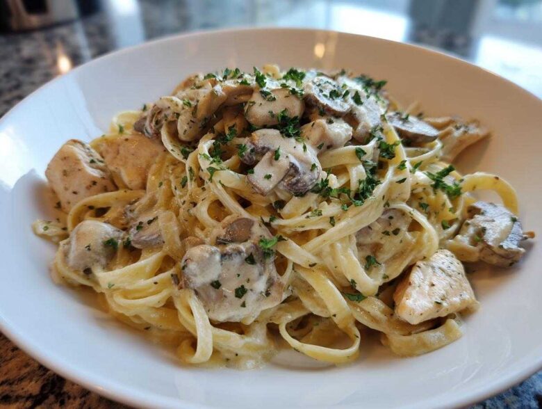 A close-up of a white bowl filled with Creamy Mushroom Chicken Pasta with Garlic Sauce, garnished with fresh parsley.