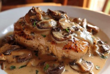 A perfectly seared chicken breast smothered in a rich, creamy mushroom sauce and garnished with parsley.