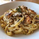 Close-up of fettuccine pasta tossed in a creamy sauce with sliced mushrooms, pieces of seared chicken, and fresh thyme, representing Creamy Mushroom Garlic Pasta with Chicken.