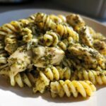 A close-up of Creamy Pesto Chicken Pasta with Mozzarella featuring fusilli pasta coated in green pesto sauce and chunks of chicken.