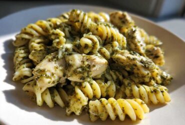 A close-up of Creamy Pesto Chicken Pasta with Mozzarella featuring fusilli pasta coated in green pesto sauce and chunks of chicken.