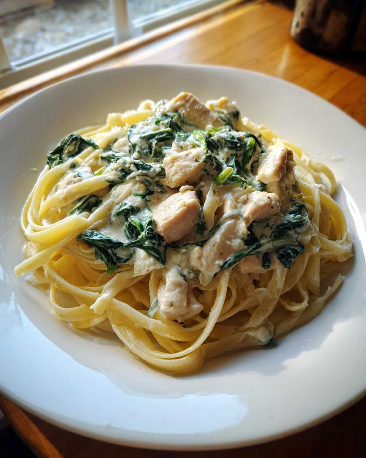 A serving of Creamy Spinach Alfredo Pasta with Chicken tossed with fettuccine noodles, served on a white plate.