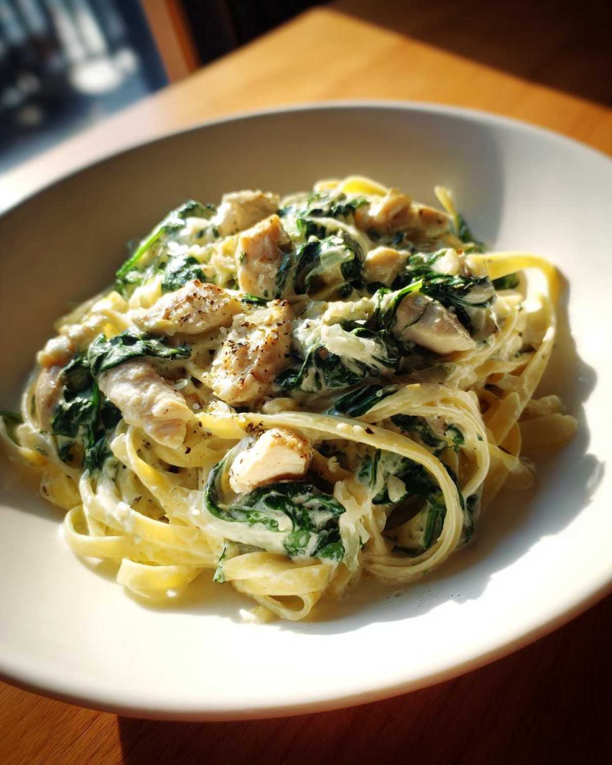 A close-up serving of rich Creamy Spinach Alfredo Pasta with Chicken tossed in a white bowl.